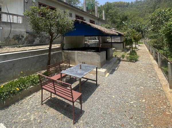 The row of rooms with an outdoor sitting area and a gravel path running past it toward the hill